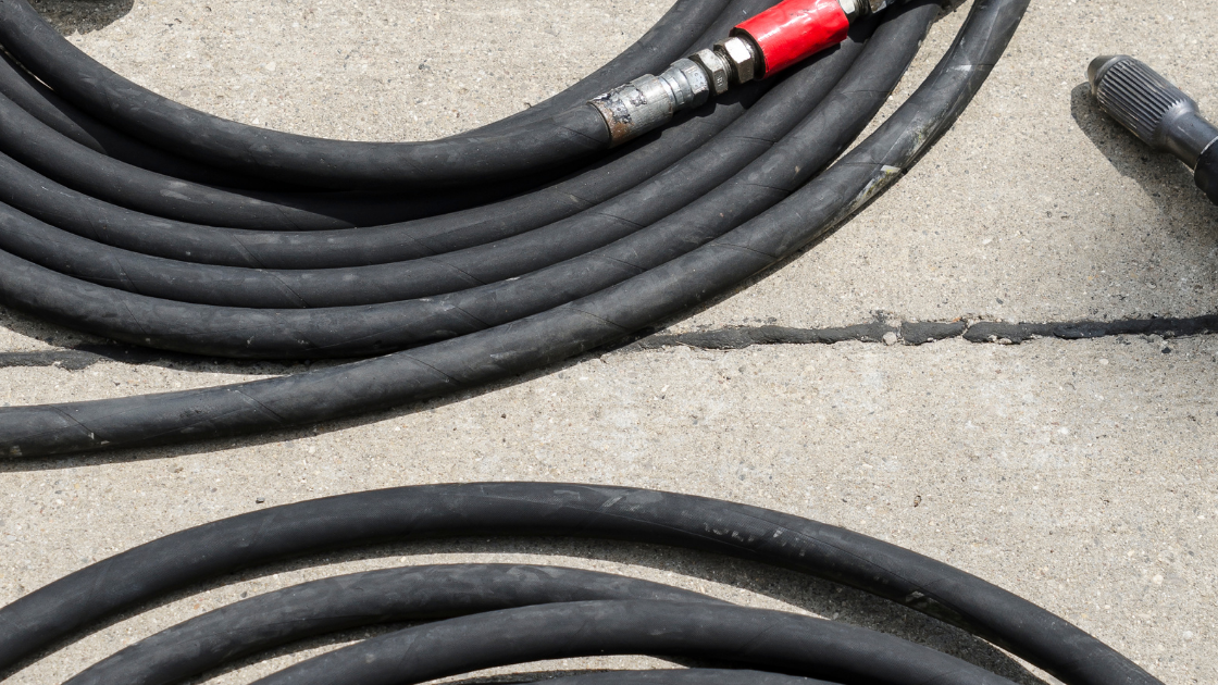 Coiled black rubber hoses with metal connectors on a concrete surface.