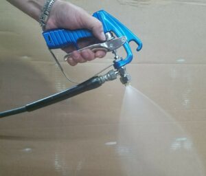 A person holding a handheld spray gun with a blue grip, spraying a fine mist of liquid.