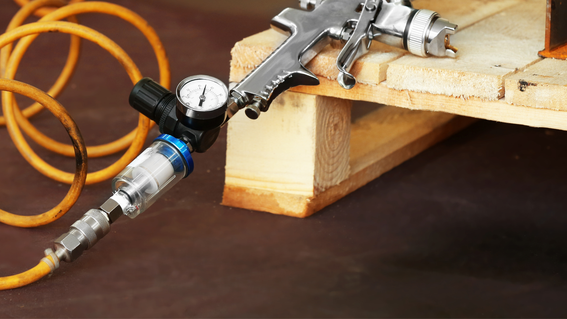 Air spray gun connected to a pressure regulator and hose on a wooden surface.