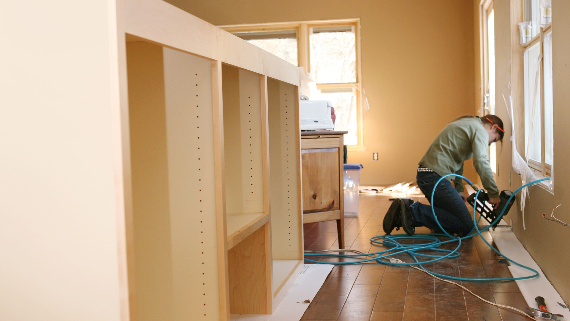 Cabinet maker using adhesive spraying equipment in a workshop setting with wooden cabinetry.
